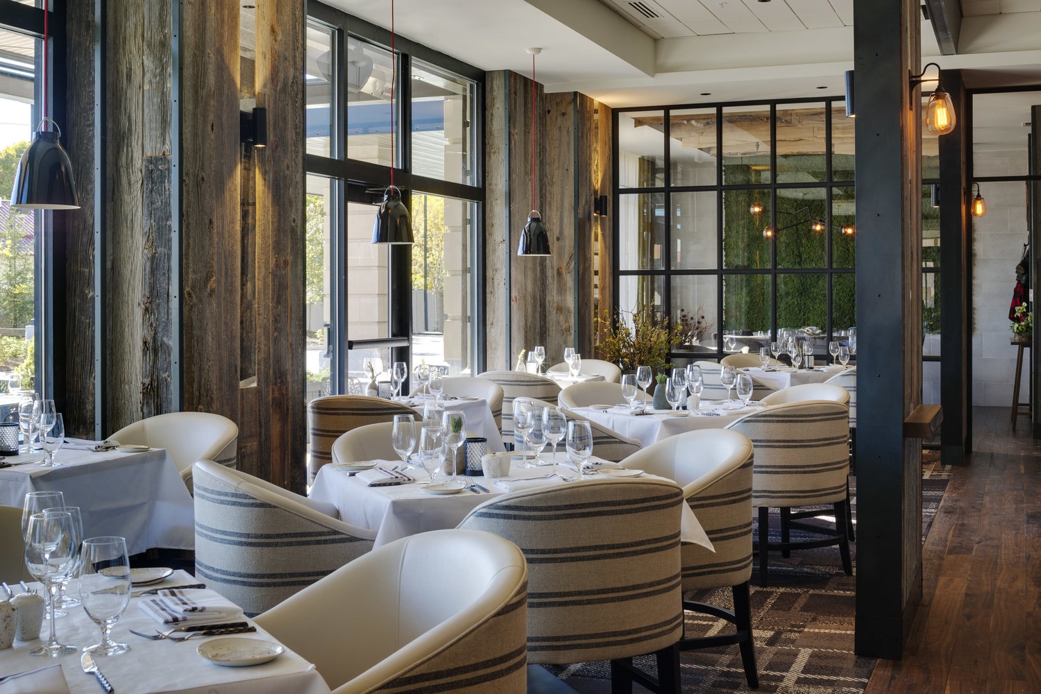 The dining room set with white chairs and warm lighting under tall windows.
