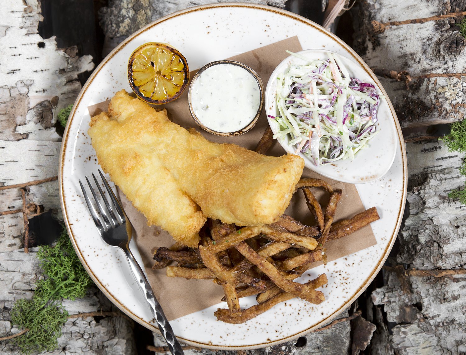 Battered fish and fries with slaw and tartar, served on a slab of birch bark.
