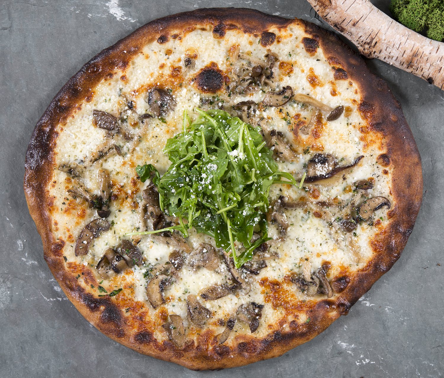 An overhead view of a wood-fired mushroom pizza topped with arugula.