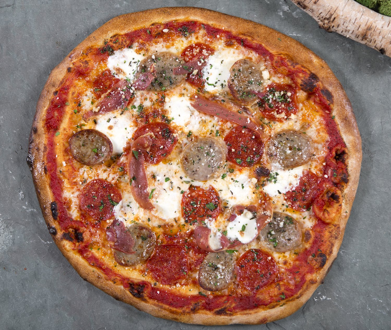 An overhead view of a pizza with sausage, pepperoni and fresh basil.