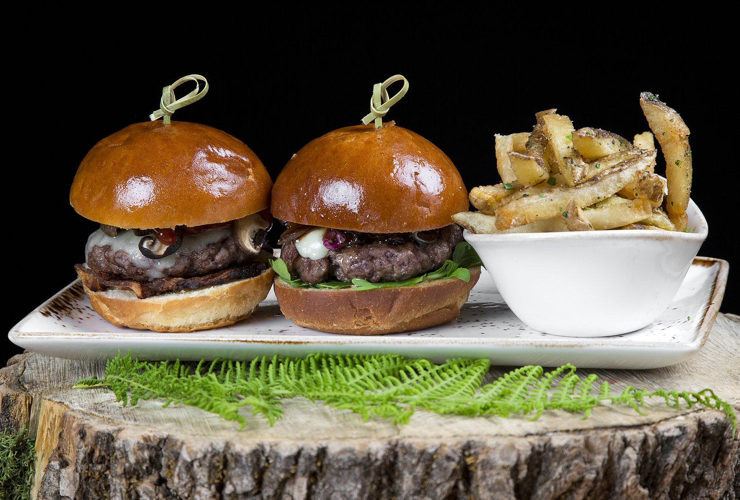 Three small burgers on brioche buns with a side of fries on a log round.